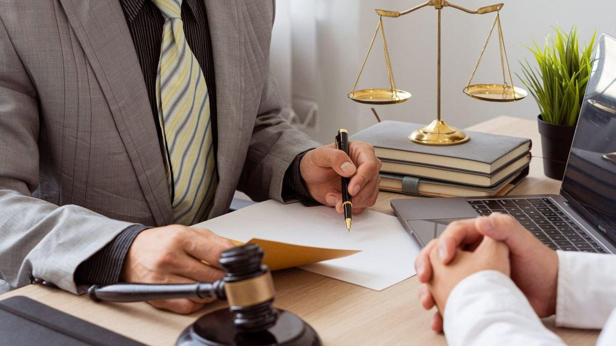 Lawyers discuss business contract documents sitting at a desk in the office of conceptual legal advice. Counselor with hammers and scales of justice on the table.