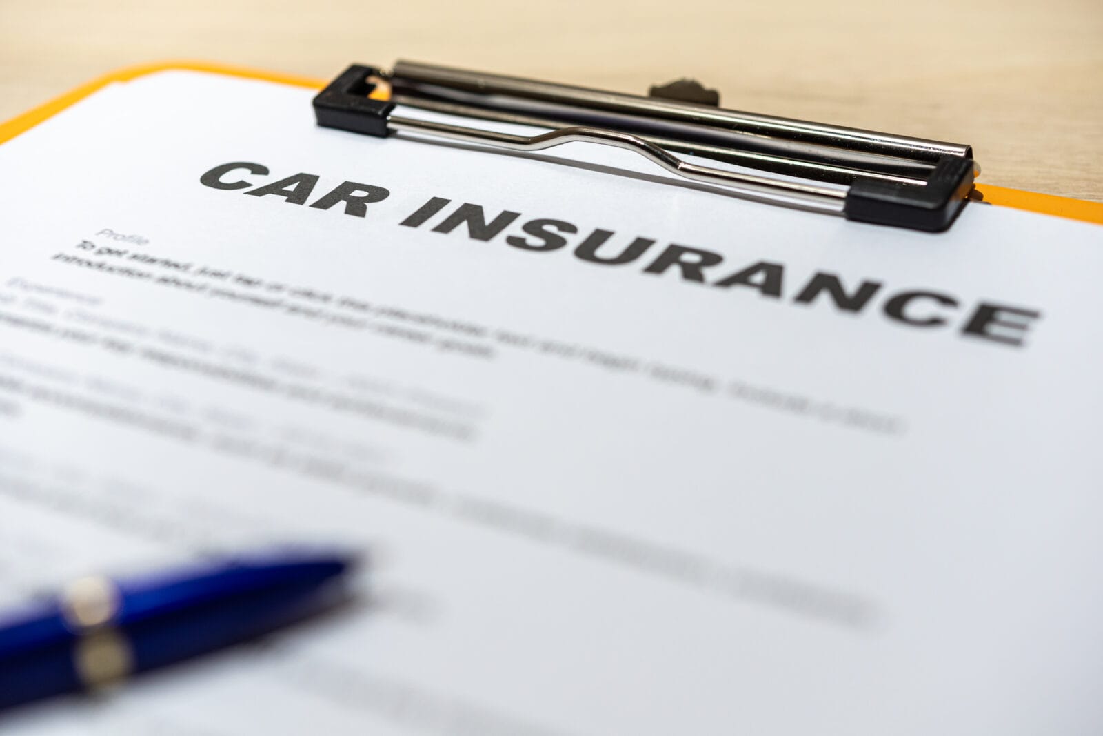 Close-up of a car insurance form on a clipboard with a blue pen on a desk.